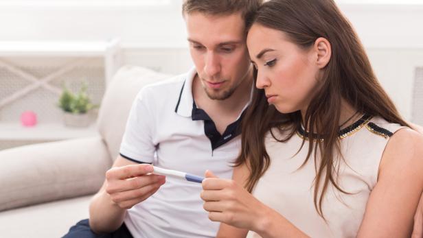 Ein Mann und eine Frau schauen enttäuscht auf einen Schwangerschaftstest.