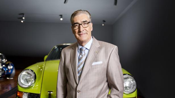 Johannes Hödlmayr steht vor einem grünen Porsche in einem hellen Anzug