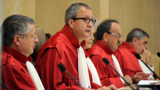 Mehrere Richter in roten Roben sitzen an einem Tisch mit Mikrofonen.