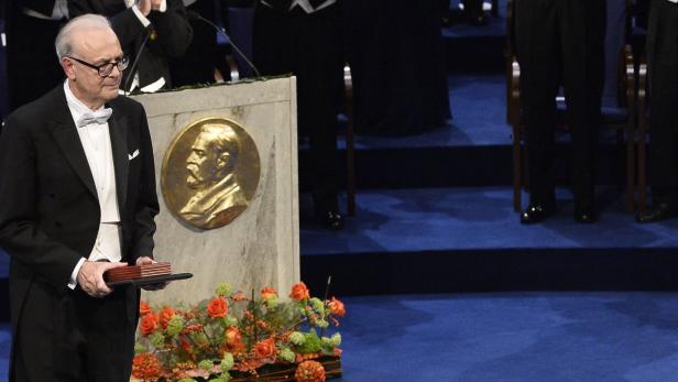 Ein Mann im Smoking hält eine Auszeichnung neben einem Denkmal von Alfred Nobel.