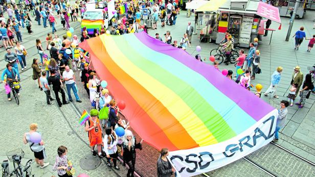 Eine Menschenmenge hält eine riesige Regenbogenflagge beim CSD Graz.