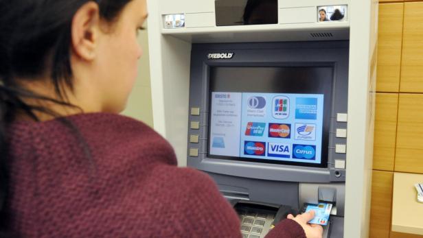 Eine Frau hebt mit einer Bankkarte Geld an einem Geldautomaten ab.