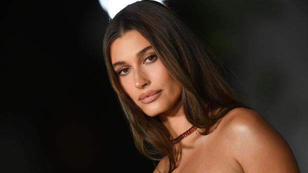 Porträt von Hailey Bieber mit braunen Haaren und einer orangefarbenen Halskette.