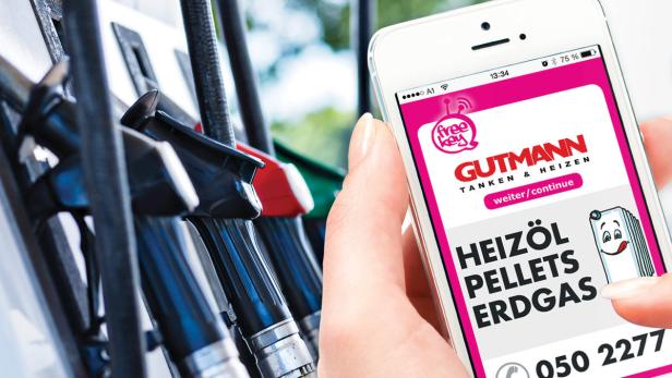 Eine Hand hält ein Smartphone mit der Gutmann-App an einer Tankstelle.