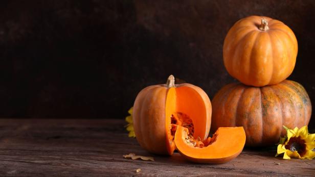Mehrere Kürbisse und Sonnenblumen auf einem Holztisch.