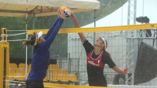 Zwei Beachvolleyballspielerinnen kämpfen im Regen um den Ball am Netz.
