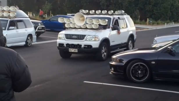 Ein weißer Ford Explorer mit vielen Lautsprechern auf dem Dach steht auf einem Parkplatz.