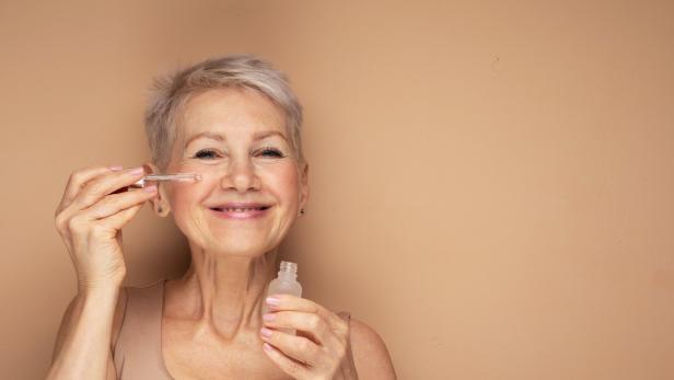 Eine ältere Frau trägt ein Serum mit einer Pipette auf ihr Gesicht auf.