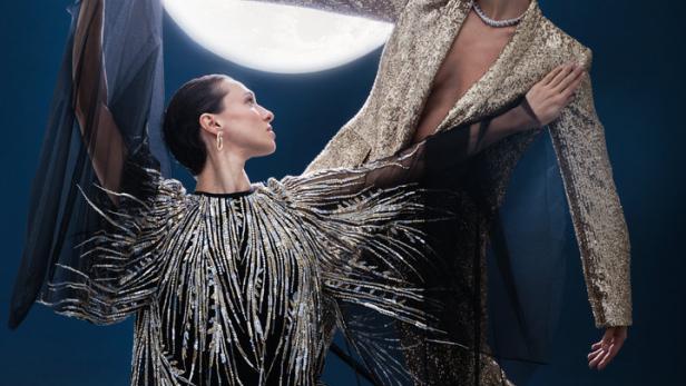 Zwei Frauen in glitzernden Kleidern posieren vor einem großen Mond.