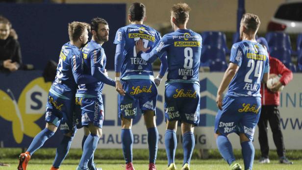 Fünf Fußballspieler in blauen Trikots feiern auf dem Spielfeld.