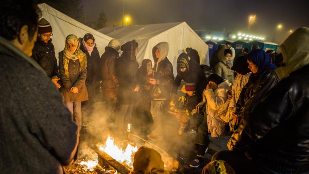 Eine Gruppe von Menschen wärmt sich nachts an einem Lagerfeuer vor Zelten.