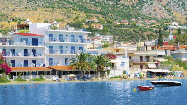 Das Hotel Aris liegt an einem Strand mit Badegästen und Booten vor einer Hügellandschaft.