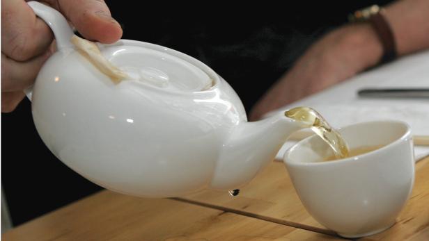 Eine Person gießt Tee aus einer weißen Teekanne in eine Tasse.