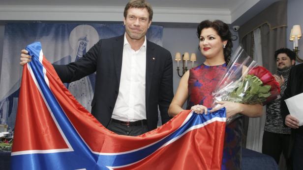 Ein Mann und eine Frau halten eine blau-weiß-rote Flagge in einem Innenraum.