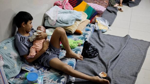 Ein Jugendlicher hält ein Baby im Arm, während sie auf einer Matratze sitzen.