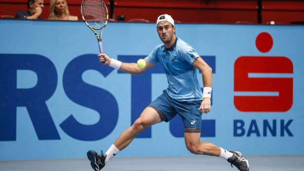 Ein Tennisspieler schlägt einen Ball vor einer Sponsorenwand.
