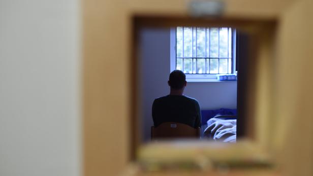 Justizanstalt: Ein Mann sitzt in einem Raum vor einem vergitterten Fenster.