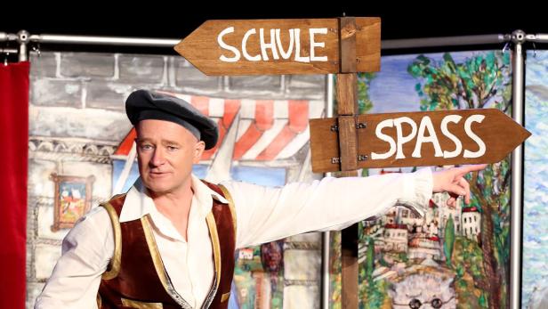 Kopie von Pinnocchio, Musical Ein Mann in Kostüm zeigt auf ein Schild mit der Aufschrift „Spass“.