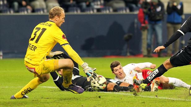 Ein Fußballtorwart in gelber Uniform versucht, einen Torschuss abzuwehren.