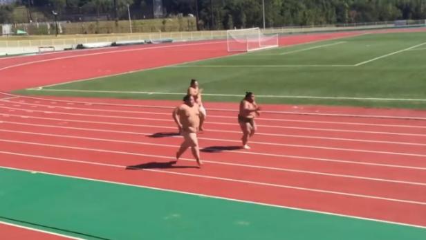 Drei Sumoringer laufen auf einer roten Tartanbahn.