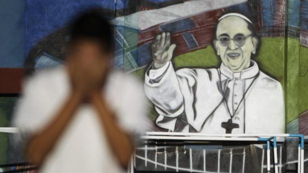 Ein Wandgemälde von Papst Franziskus, vor dem eine verschwommene Person steht.