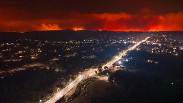 Nachts brennt ein Waldbrand über einer beleuchteten Stadt.