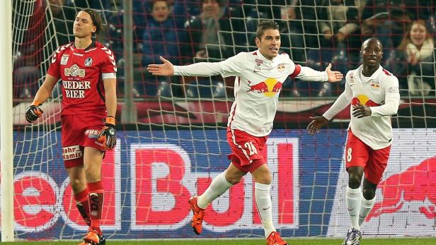 Ein Fußballspieler jubelt, während zwei andere Spieler im Hintergrund stehen.