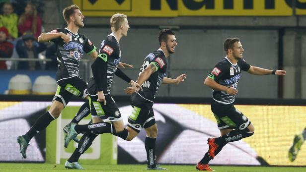 Vier Fußballspieler in schwarz-weißen Trikots jubeln auf dem Spielfeld.