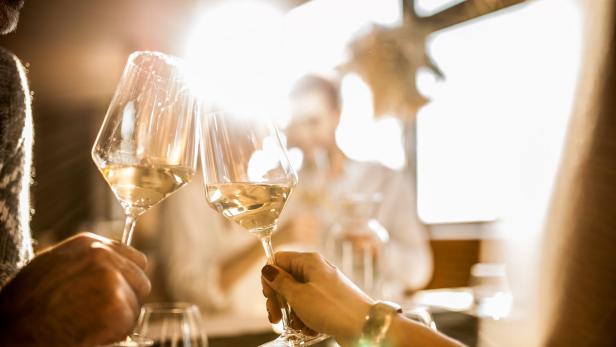 Zwei Personen stoßen mit Weißweingläsern an.