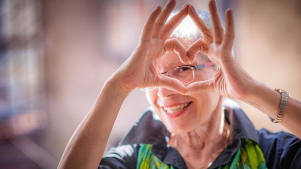 Eine ältere Frau formt mit ihren Händen ein Herz.