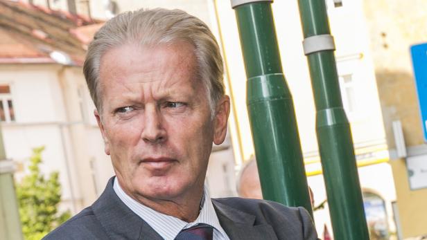 Ein Mann im Anzug steht im Freien vor einem Gebäude.