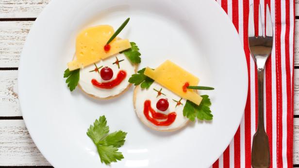 Zwei Kekse sind als Clowns mit Käse, Johannisbeeren und Kräutern verziert.