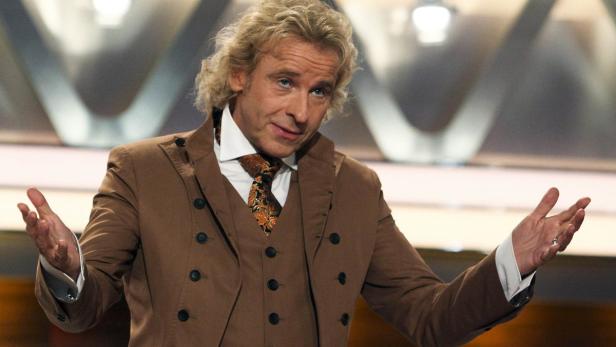 Thomas Gottschalk in einem braunen Anzug gestikuliert auf einer Bühne.