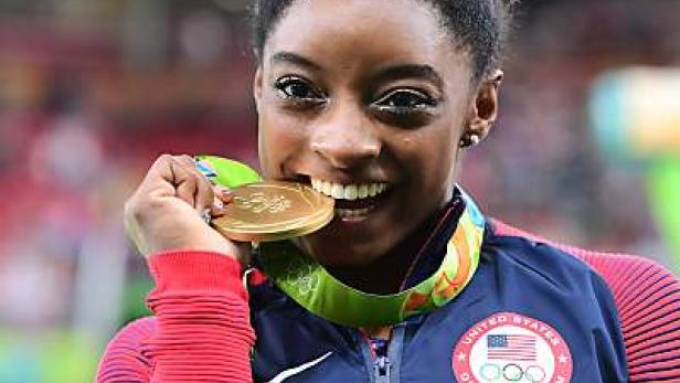 Simone Biles beißt in ihre Goldmedaille.