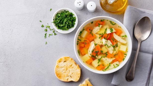 Eine Schüssel Hühnersuppe mit Karotten, Kartoffeln und Petersilie, dazu Brot.