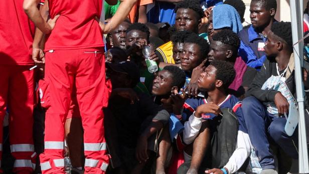 Migranten hocken vor einem Mann des Roten Kreuzes