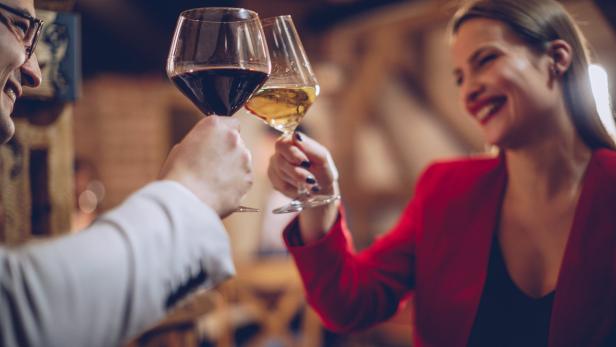 Ein Paar stößt mit Rot- und Weißwein in einem Restaurant an.