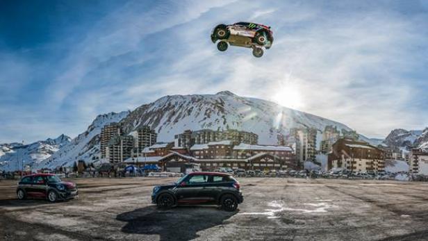 Ein Rennwagen springt vor einer verschneiten Bergkulisse in der Luft.