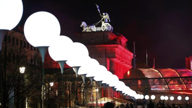 Das Brandenburger Tor in Berlin ist nachts rot beleuchtet, mit einer Reihe von Kugellampen im Vordergrund.