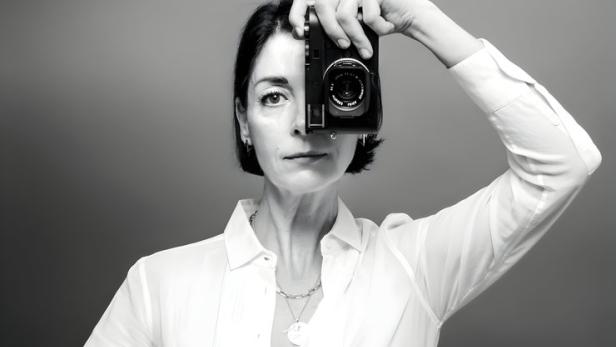 Mary McCartney hält eine Kamera vor ihr Auge und trägt eine Schürze mit Kochutensilien.