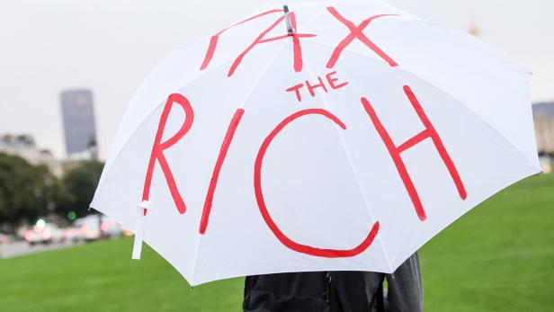 Protestierende für Vermögenssteuer mit Schirm, auf dem "Tax the rich" draufsteht