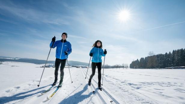 Ein Mann und eine Frau laufen an einem sonnigen Tag Ski durch eine verschneite Landschaft.