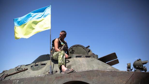 Ein ukrainischer Soldat sitzt mit der ukrainischen Flagge auf einem Panzer.