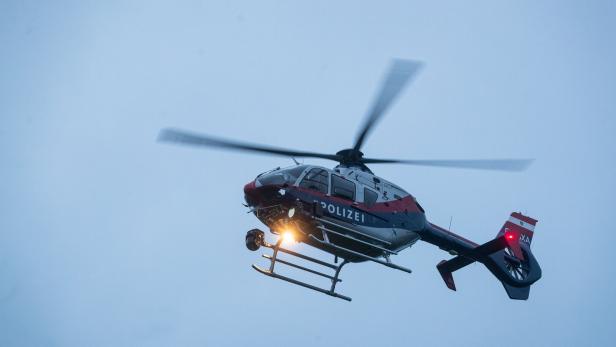 Ein Polizeihubschrauber mit eingeschaltetem Suchscheinwerfer fliegt am Himmel.
