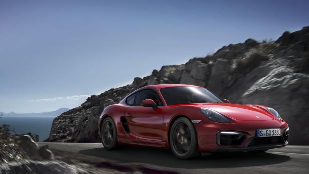 Ein roter Porsche Cayman fährt auf einer Küstenstraße.