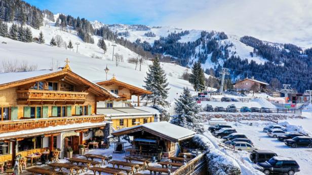 Ein Gasthof im Chalet-Stil vor einer verschneiten Berglandschaft mit Skipisten.