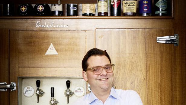 Ein Mann mit Brille steht vor einer Bar mit Getränken und Zapfhähnen.