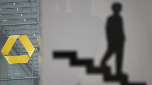 Das Commerzbank-Logo an einer Glasfassade, daneben der Schatten einer Person auf einer Treppe.