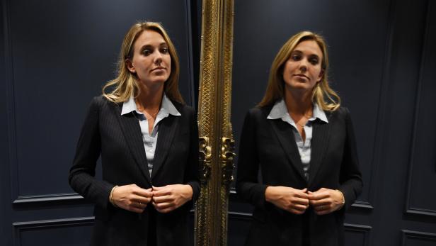 Eine Frau im Hosenanzug betrachtet sich in einem verzierten Spiegel.