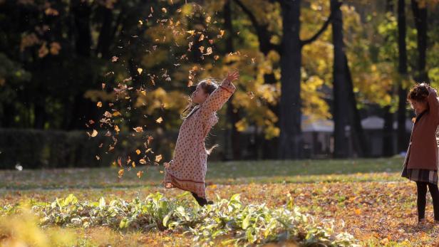 Ein Mädchen wirft im Herbstlaub Blätter in die Luft.